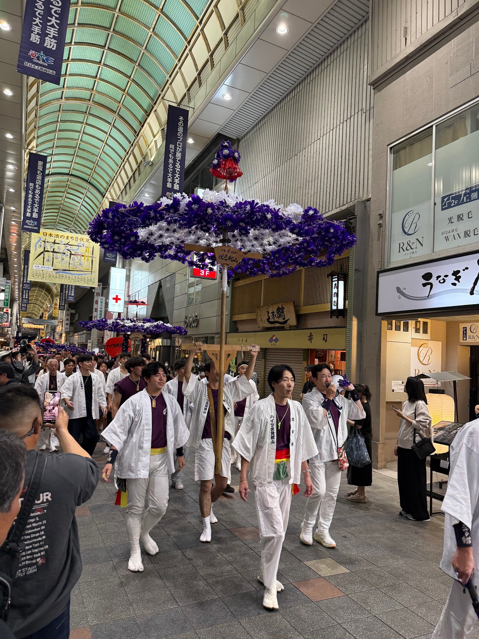 大手筋商店街裡，穿著祭典服裝的隊伍扛著紫白色大花傘遊行